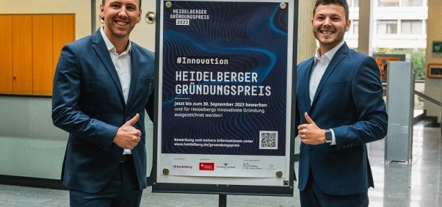 Zwei Männer stehen vor einem Flipchart, auf dem ein Plakat zum Heidelberger Gründungspreis angepinnt ist.
